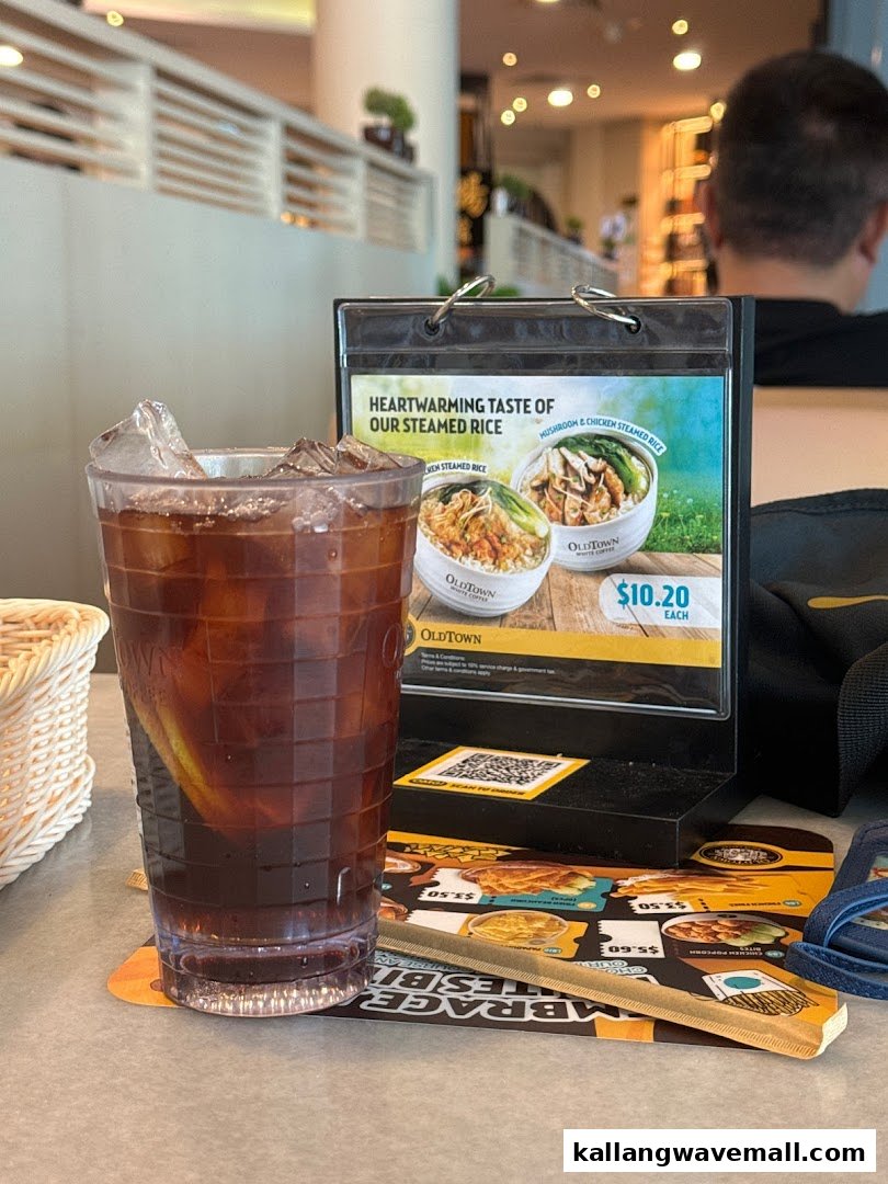 A refreshing iced drink on a table next to a promotional display for steamed rice dishes at Oldtown White Coffee.