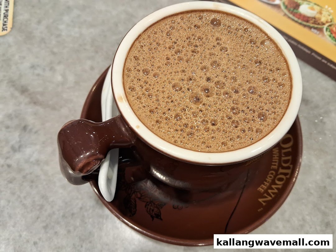A close-up of a frothy hot beverage in an Oldtown White Coffee branded cup.