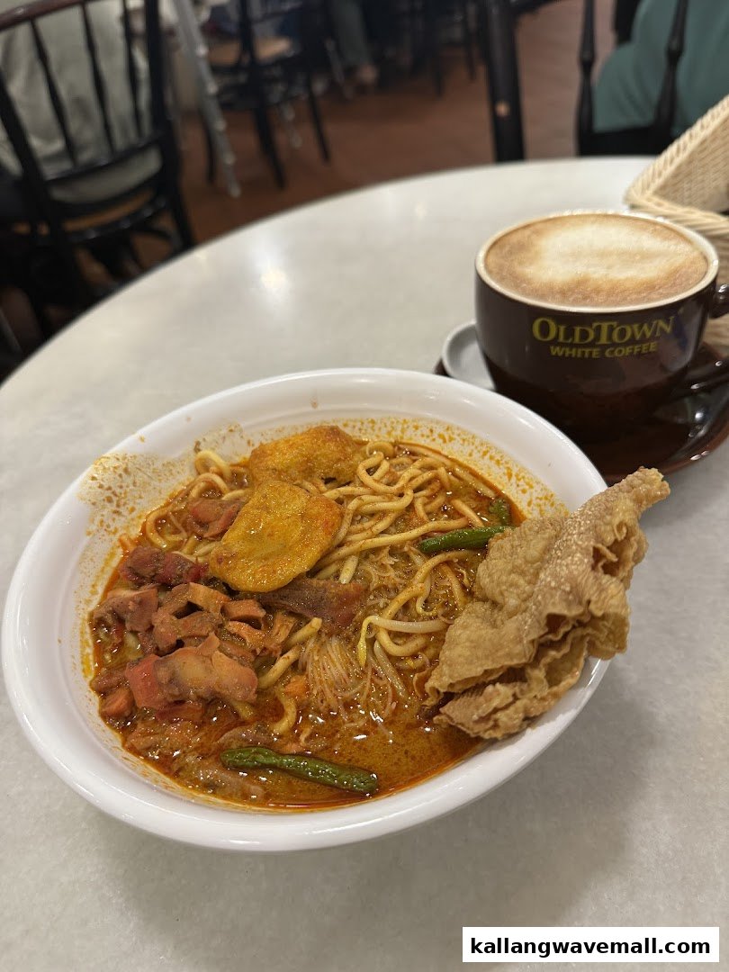 A bowl of curry noodles with crispy wonton and a cup of Oldtown White Coffee on a table.