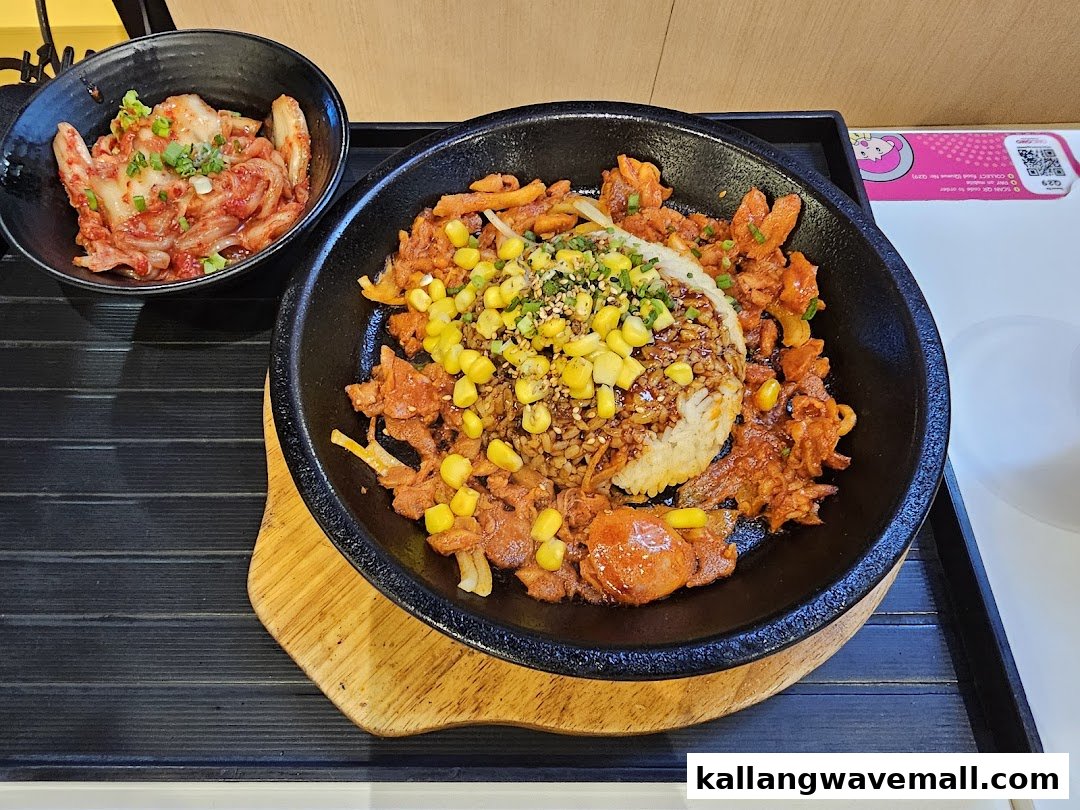 A sizzling hot plate dish with rice, spicy meat, corn, and a side of kimchi.