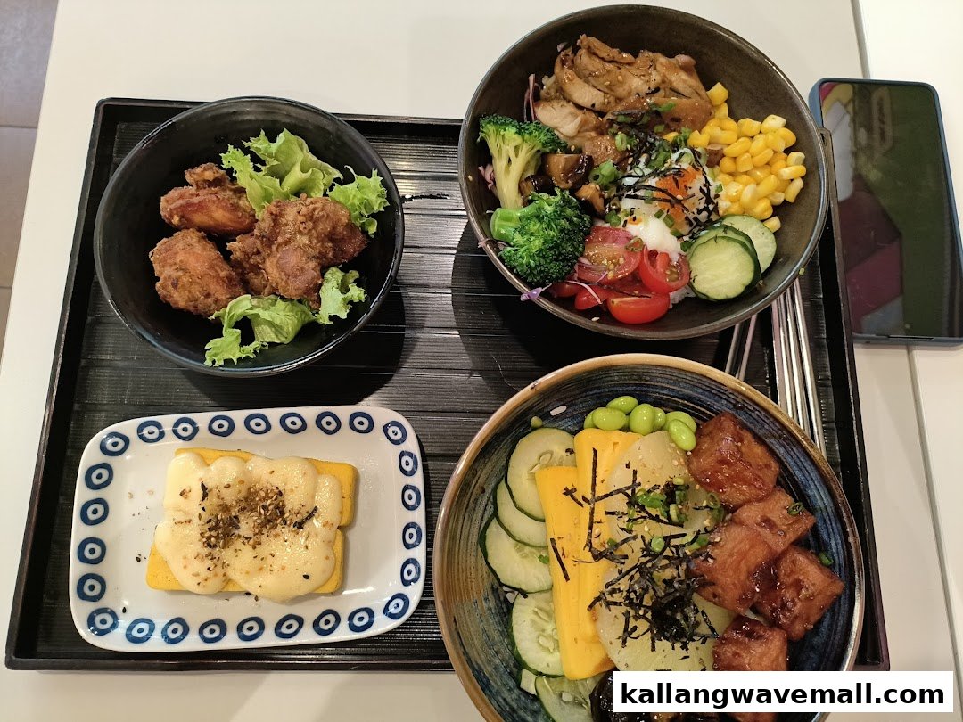 A tray featuring two vibrant rice bowls, crispy fried chicken, and a cheesy side dish.