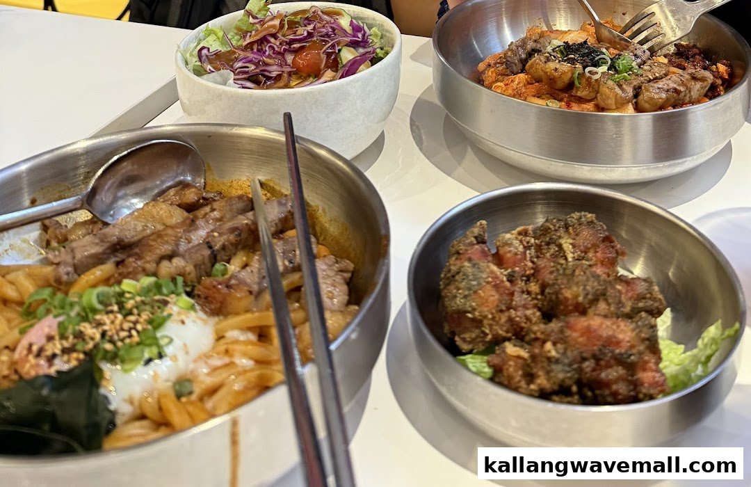 A table laden with various Korean-inspired dishes, including noodles with meat, fried chicken, and a fresh salad.
