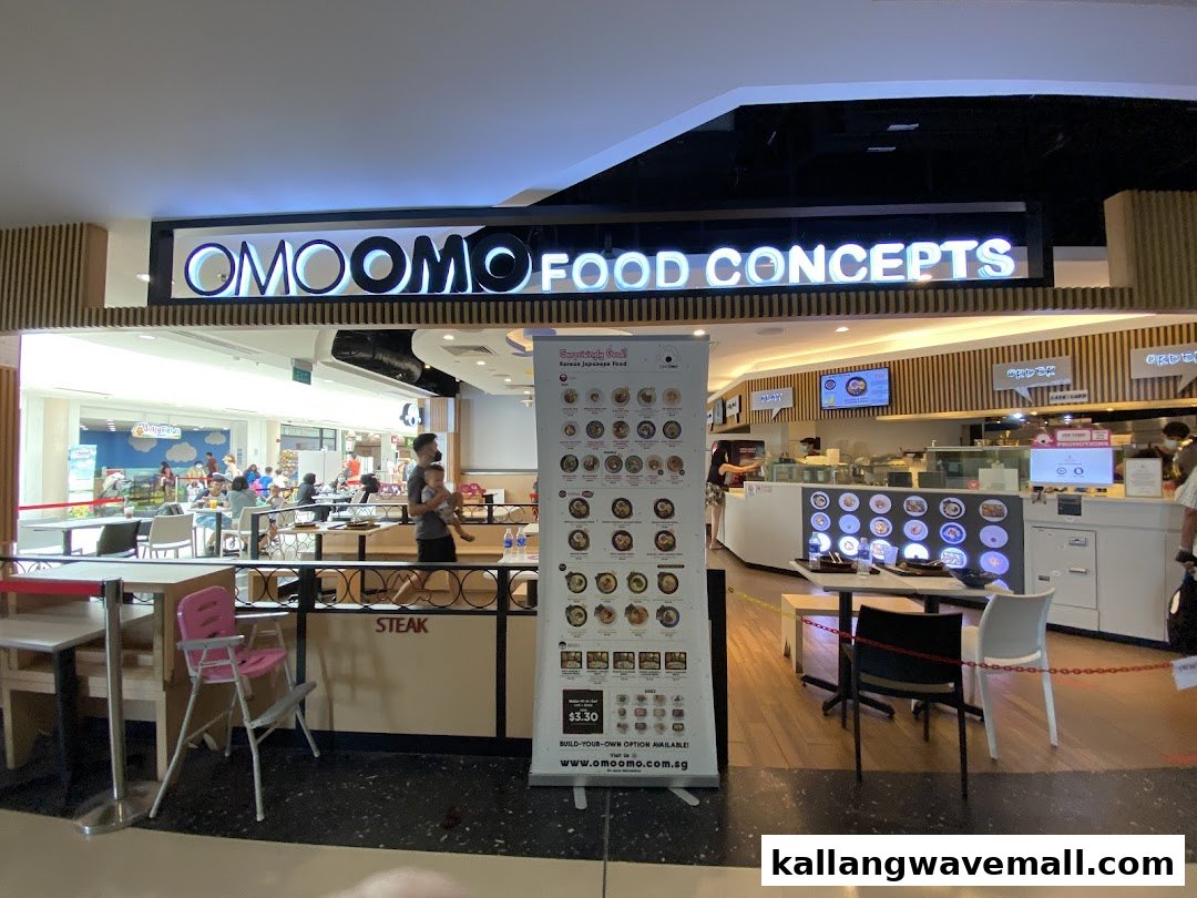 The vibrant shopfront of OMOOMO Food Concepts, featuring its illuminated sign, a menu banner, and dining area.