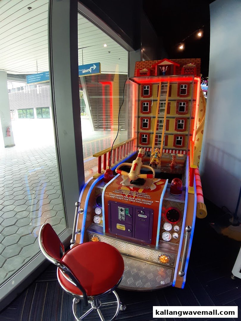 An arcade game featuring a building with a character, next to a large window, with a red stool.