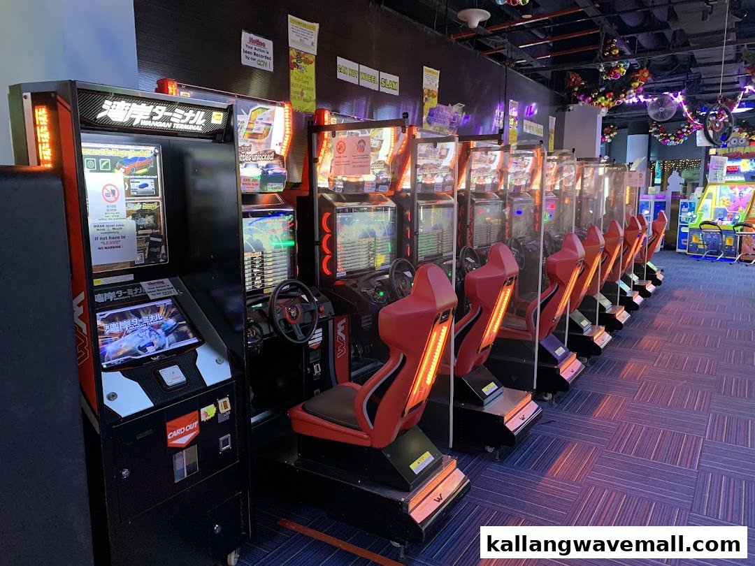 A row of racing arcade game machines with red seats inside an entertainment center.