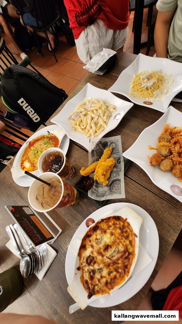 A table laden with various Italian pasta dishes, baked pasta, fried chicken, and drinks at PastaMania.