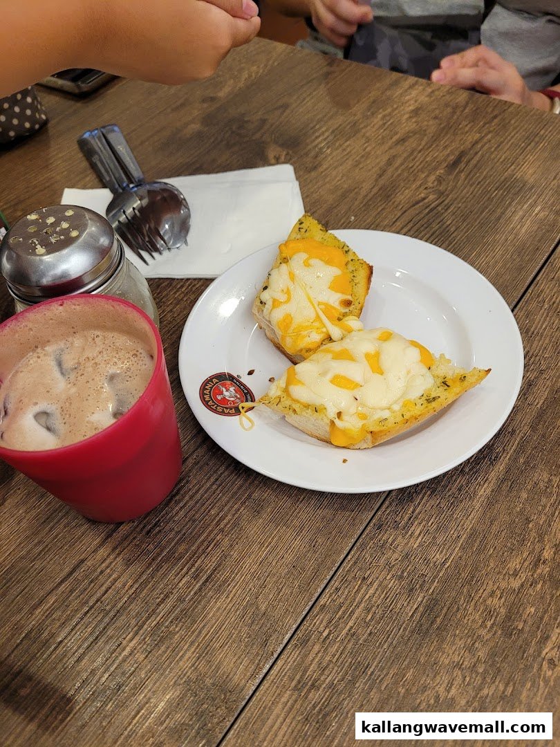 Two slices of cheesy garlic bread and a drink on a wooden table at PastaMania.