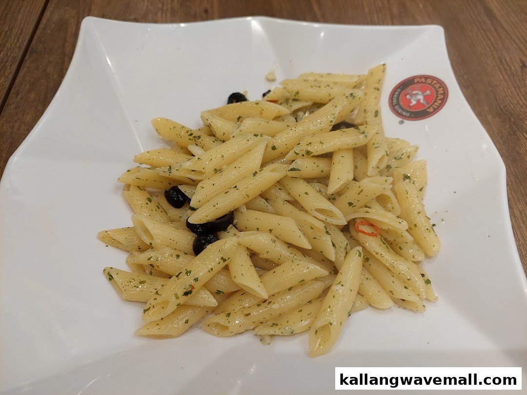 A close-up of penne pasta with herbs, black olives, and chili on a white plate.