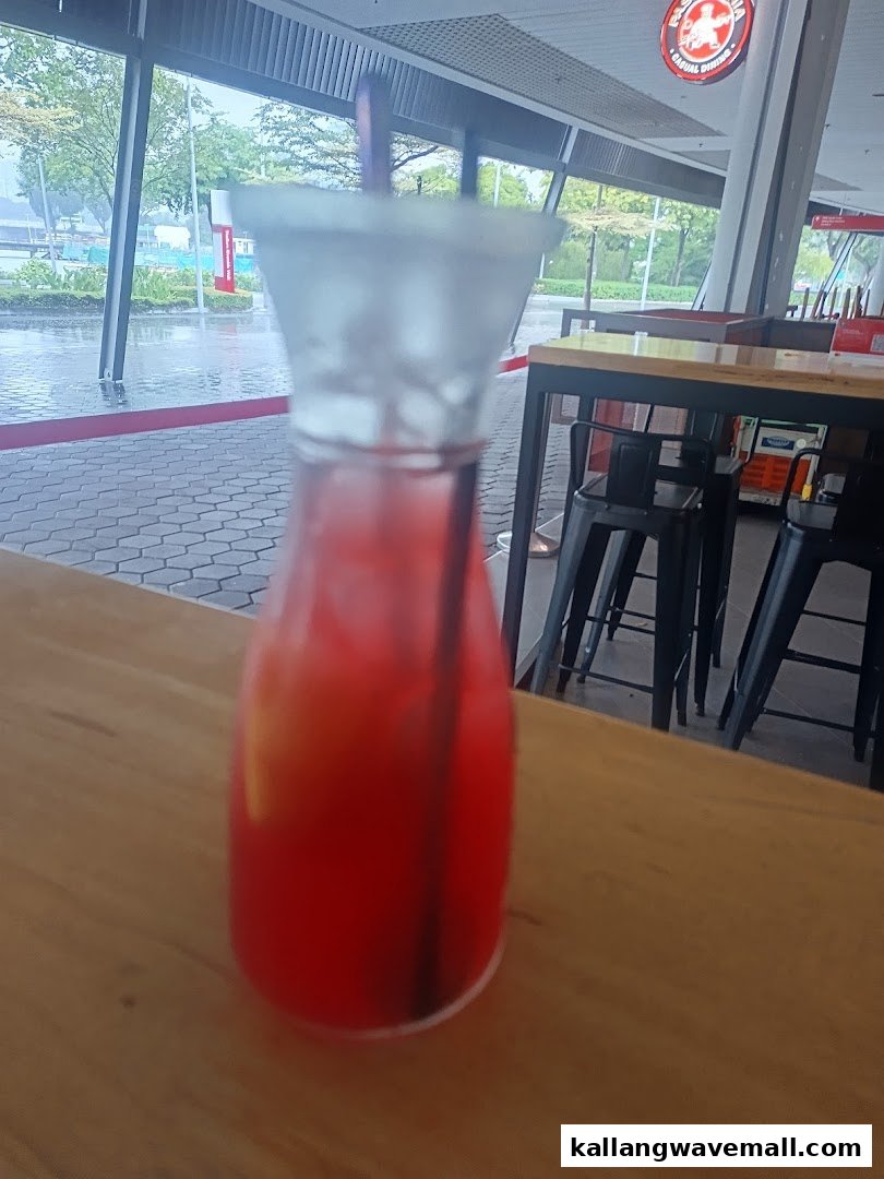 A vibrant red drink on a wooden table inside PastaMania, with an outdoor view.