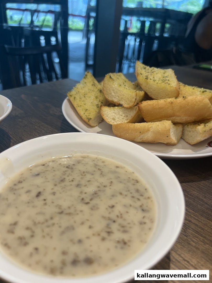 A bowl of creamy mushroom soup and a plate of golden garlic bread on a wooden table.