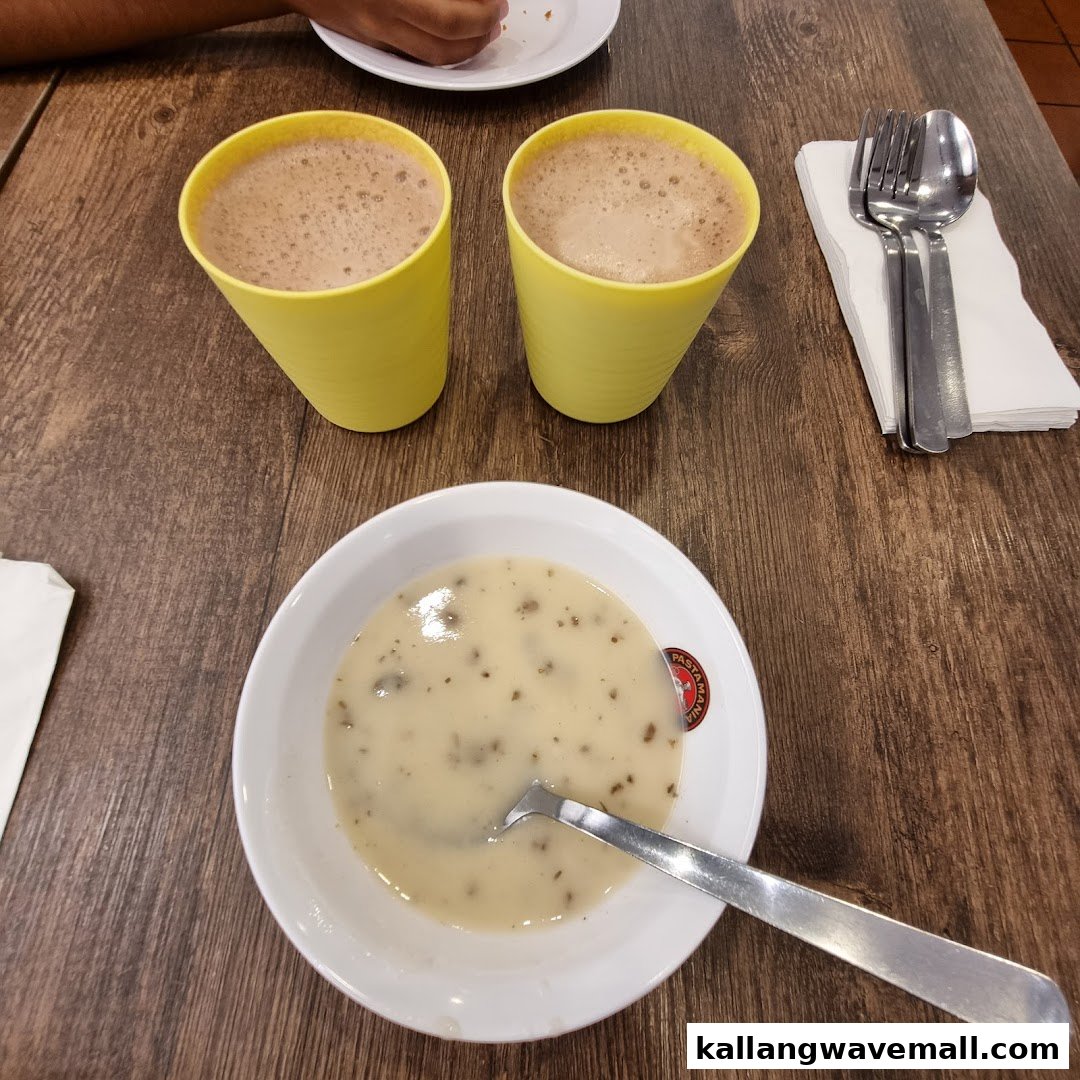 A bowl of creamy soup and two drinks in yellow cups on a wooden table at PastaMania.