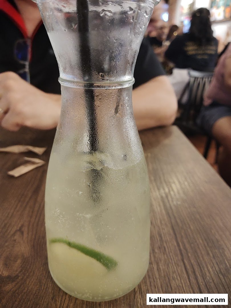 A refreshing drink with lime slices in a glass carafe on a wooden table at PastaMania.