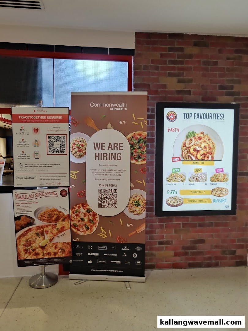 An interior view of PastaMania, showcasing promotional banners, a digital menu display, and check-in information.