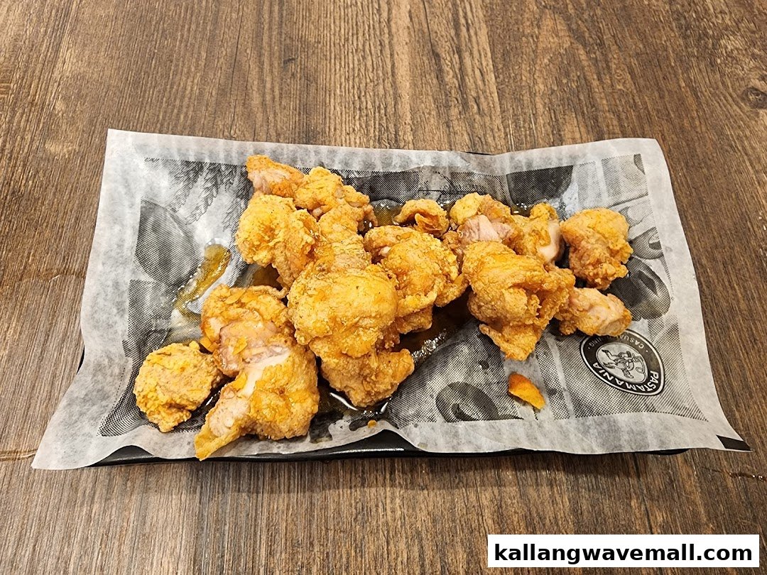 A close-up view of golden-brown fried chicken pieces served on a black plate with wax paper.