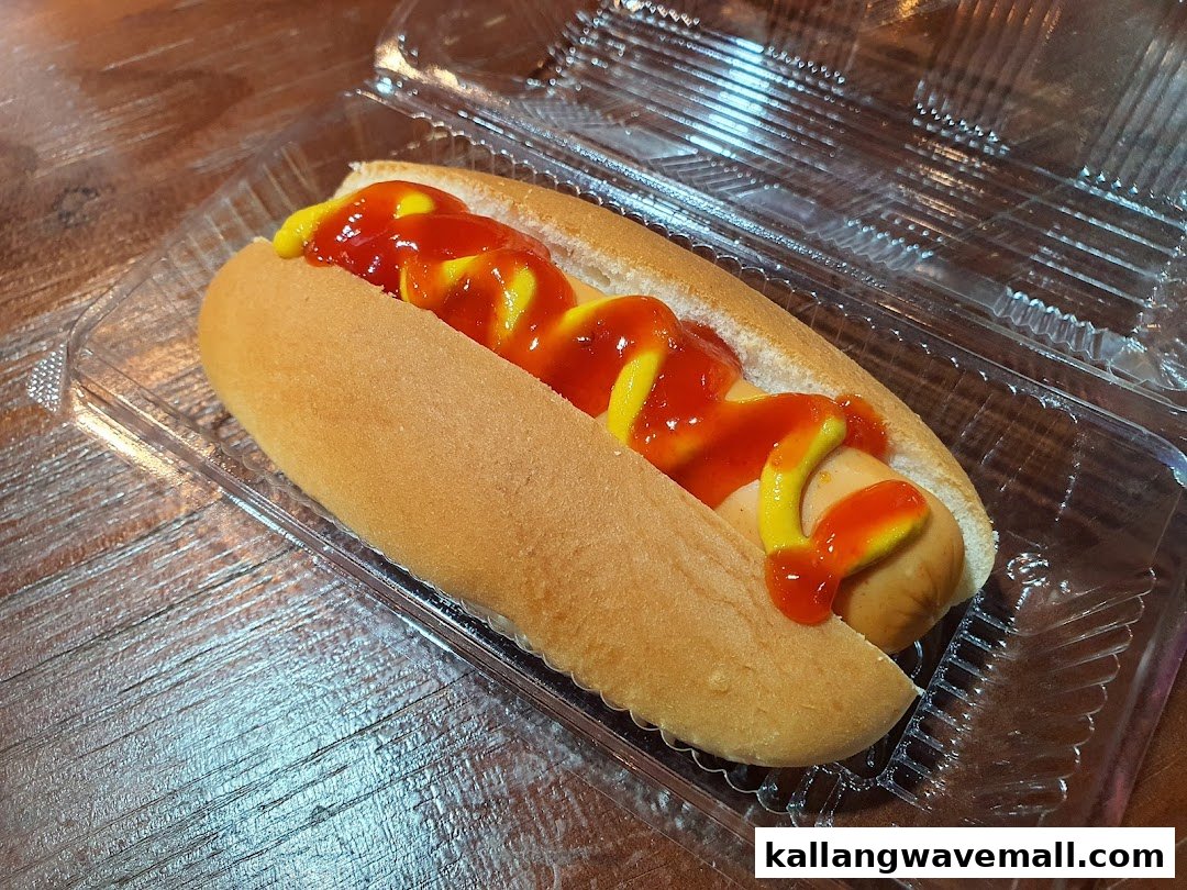 A hotdog with ketchup and mustard in a clear plastic container on a wooden surface.