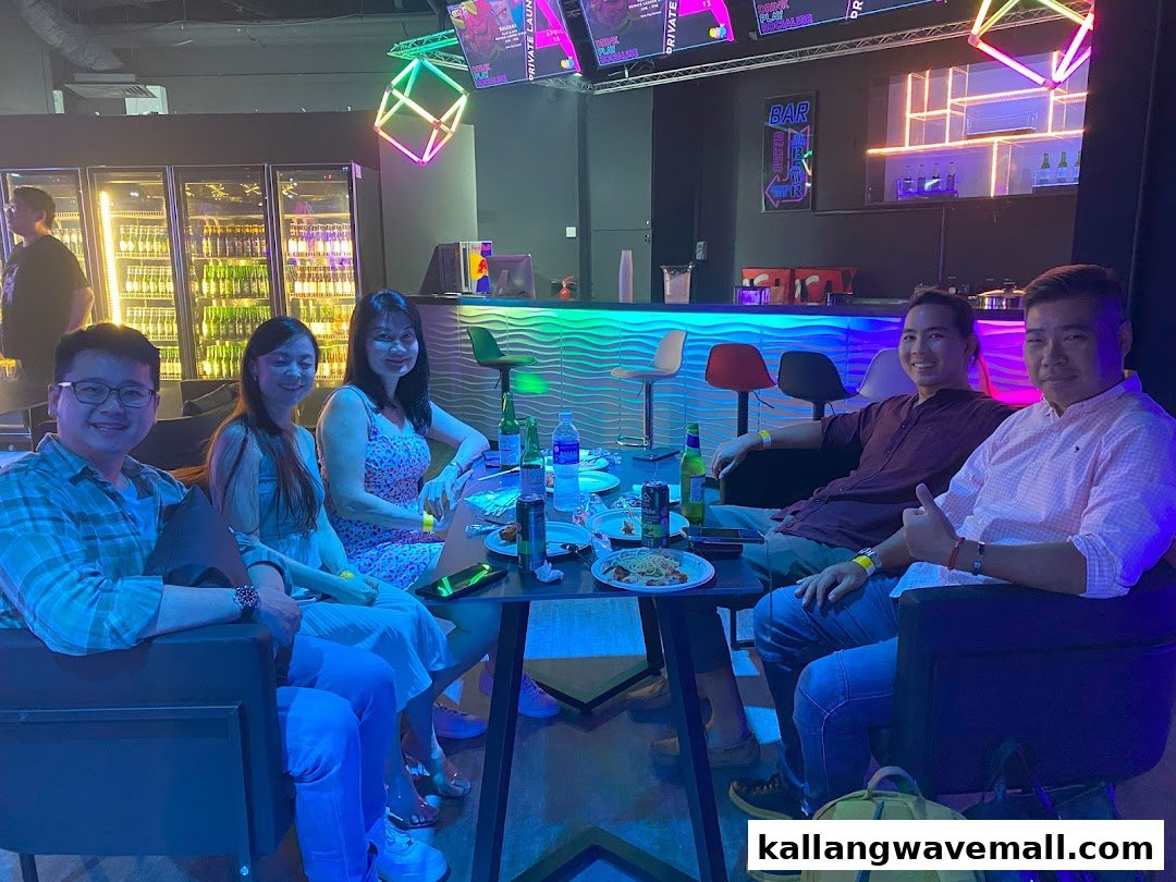A group of friends enjoying drinks and food at a vibrant, neon-lit bar and lounge area.