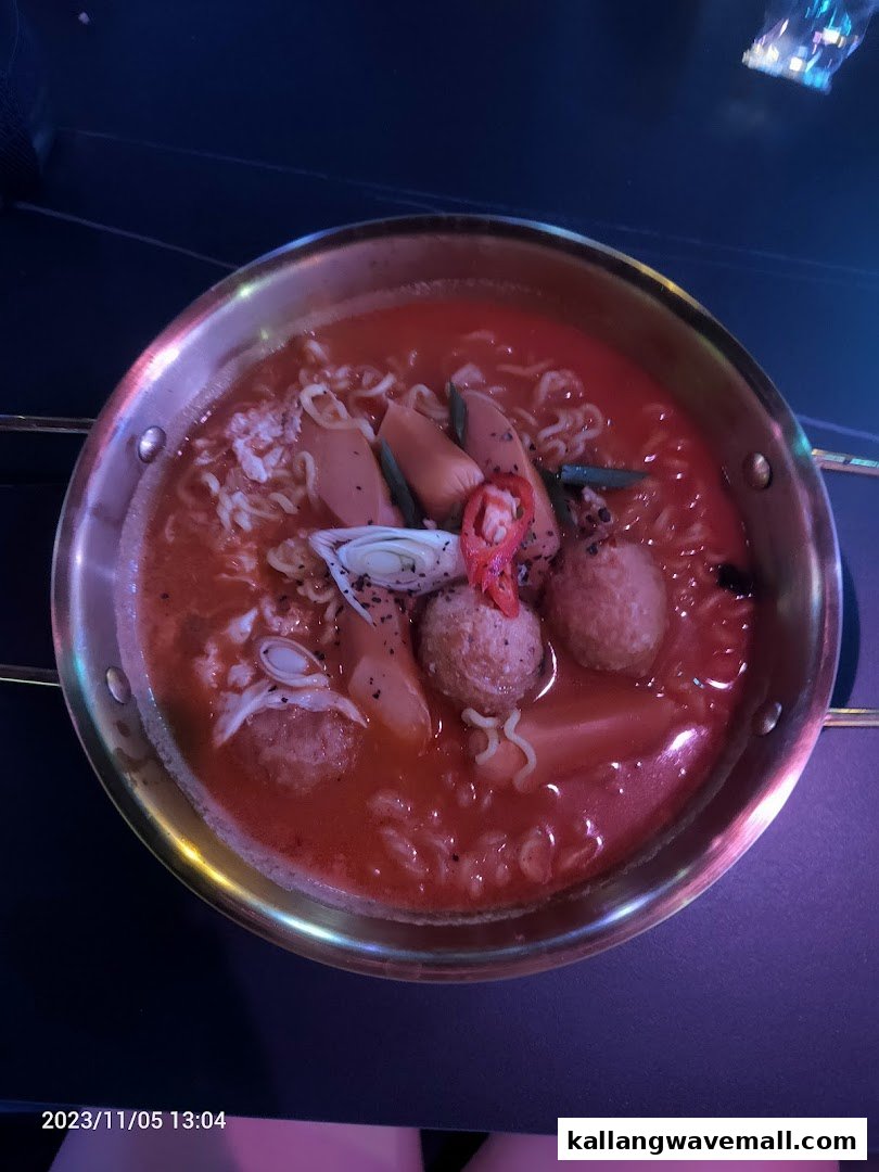 A close-up of a vibrant Korean-style stew with ramen, sausages, and meatballs in a golden pot.