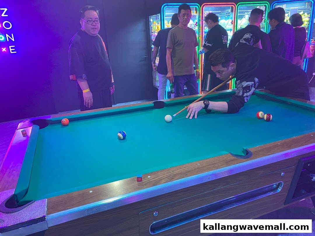 People playing pool in a vibrant entertainment center with neon lights and arcade games.