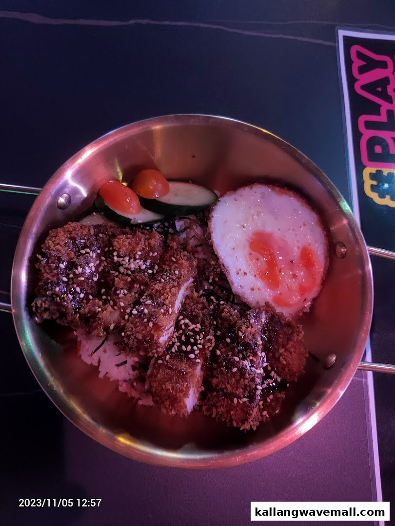 A delicious-looking katsu dish with rice, a fried egg, and vegetables served in a metal bowl.