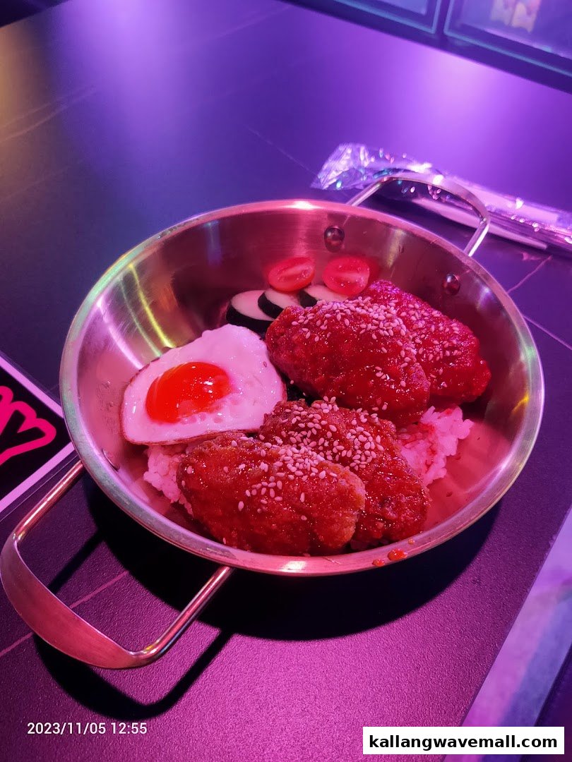 A metal pan holds Korean-style fried chicken wings with rice, a fried egg, and vegetables under purple lighting.