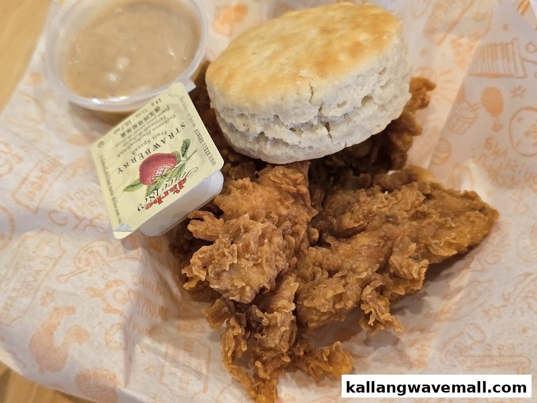 A close-up of Popeyes' crispy fried chicken, a biscuit, gravy, and strawberry jam.