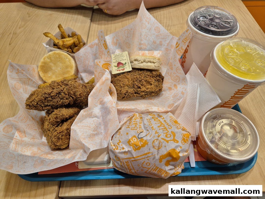 A tray filled with Popeyes fried chicken, fries, biscuits, drinks, and a wrapped burger.