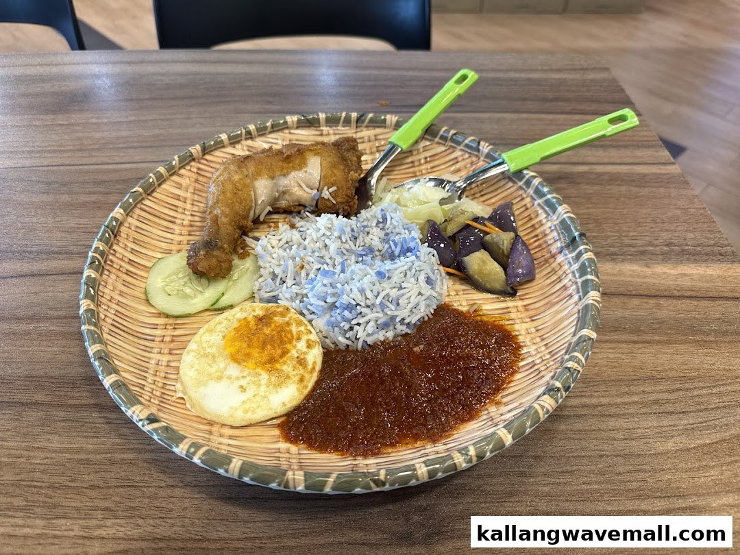 A vibrant plate of Nasi Lemak with blue pea rice, fried chicken, egg, sambal, and vegetables on a woven tray.