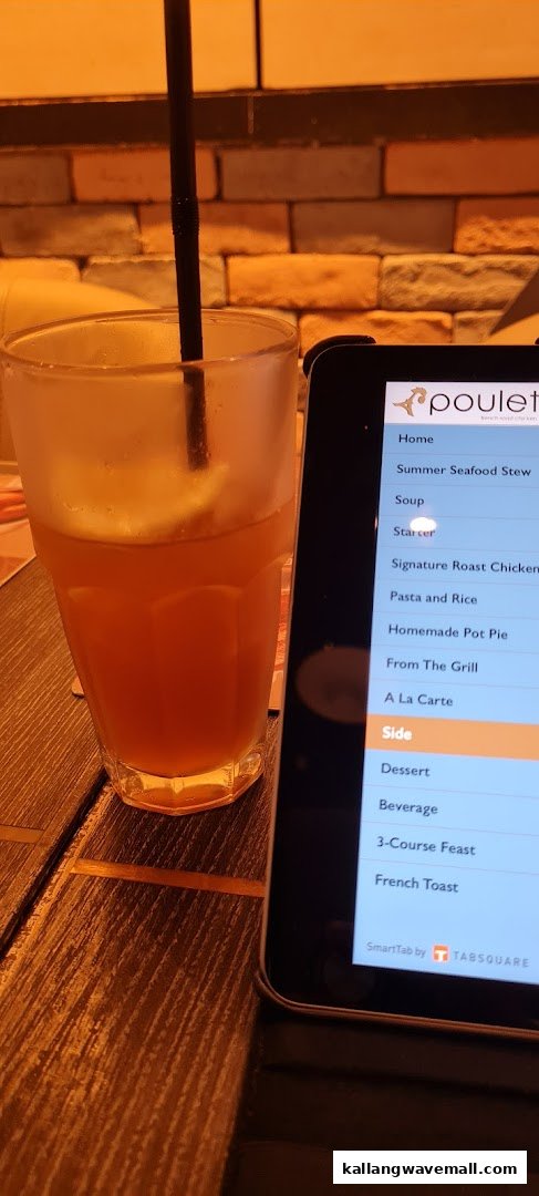 A refreshing drink next to a digital menu tablet displaying Poulet's offerings.