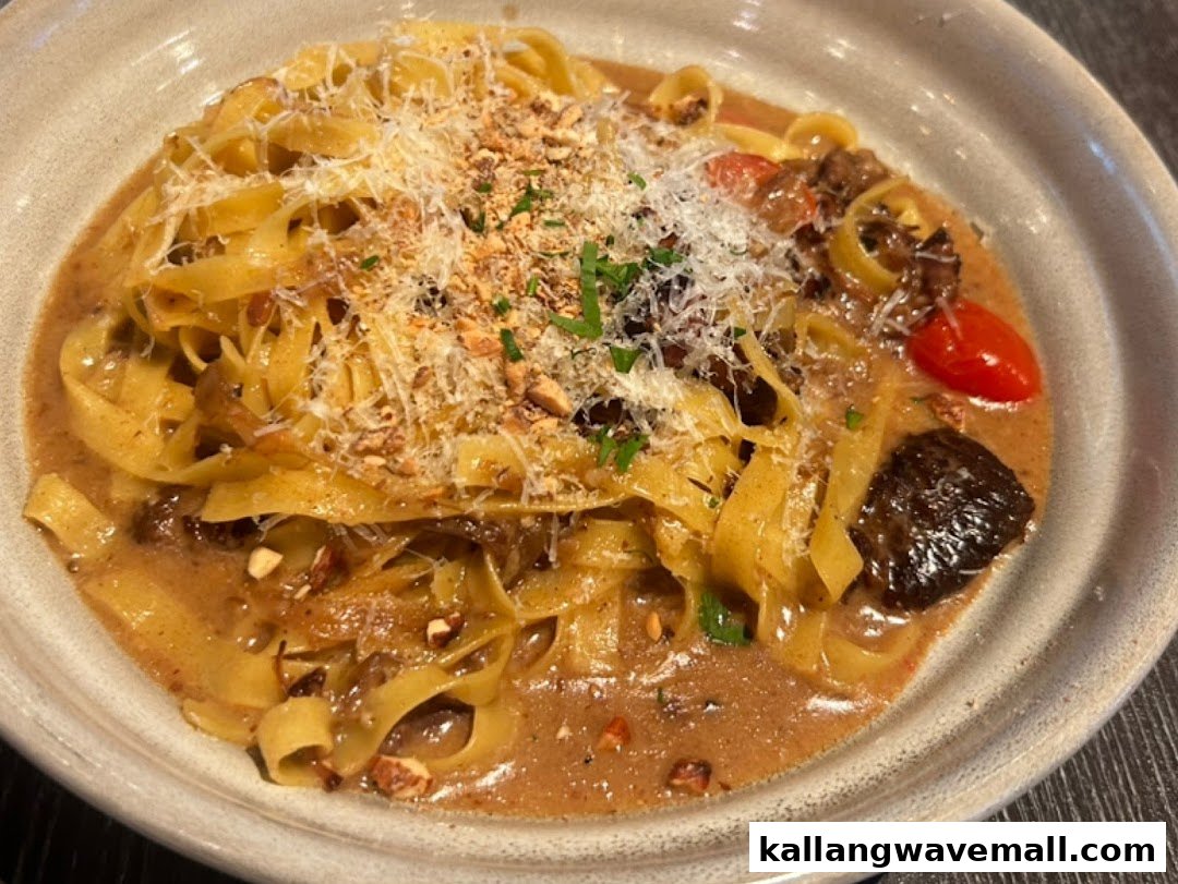A close-up of a creamy pasta dish with mushrooms, cherry tomatoes, grated cheese, and chopped nuts.