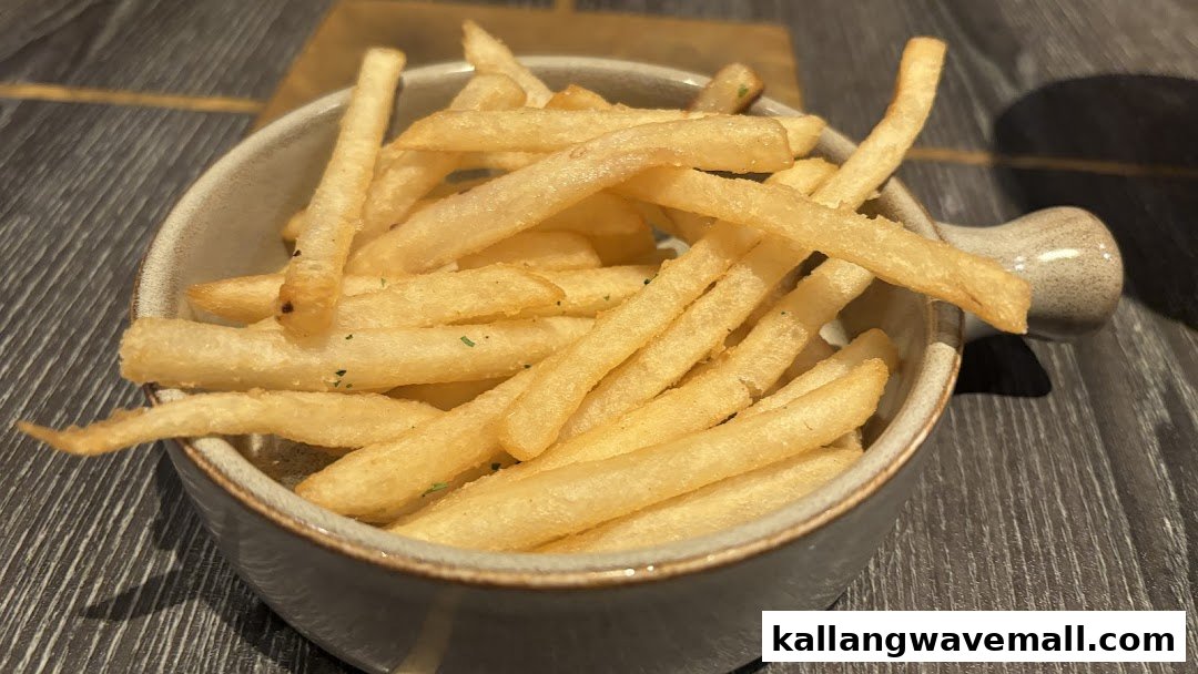 A close-up of a bowl filled with golden, crispy french fries on a dark wooden surface.