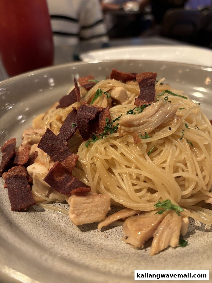 A close-up of a pasta dish with shredded chicken, crispy toppings, and fresh herbs.