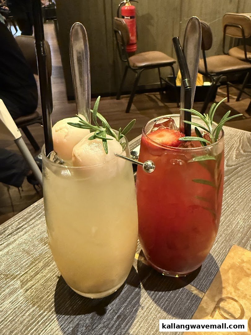 Two refreshing drinks, one lychee and one strawberry, garnished with rosemary, on a wooden table.