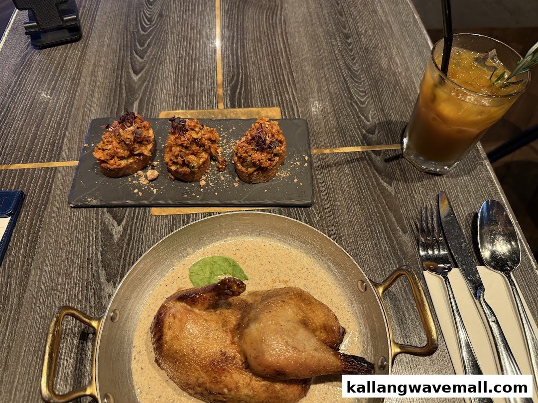 A delicious roasted chicken dish in a pan, three appetizers on a slate, and a refreshing drink on a wooden table.