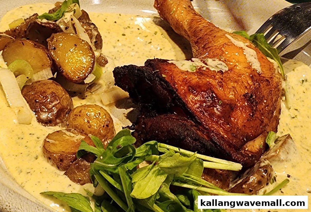 A close-up of a roasted chicken leg with potatoes, greens, and a creamy sauce on a plate.