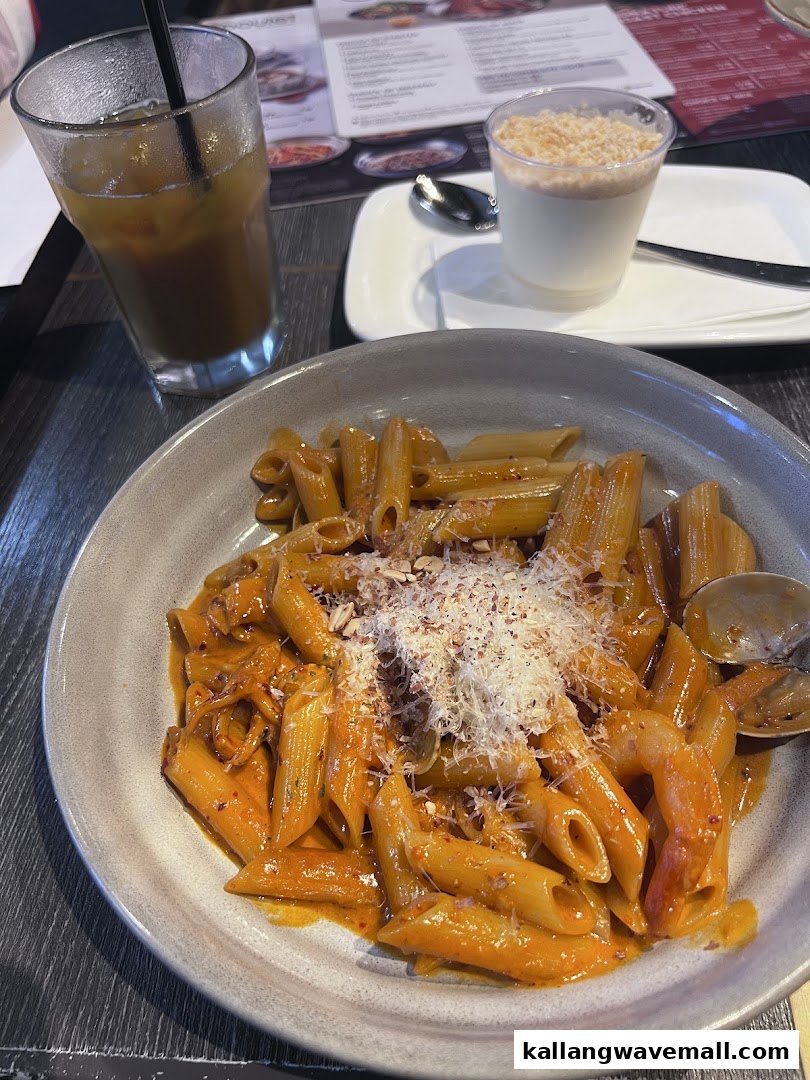 A delicious plate of pasta with a creamy sauce, topped with cheese and nuts, alongside a drink and dessert.