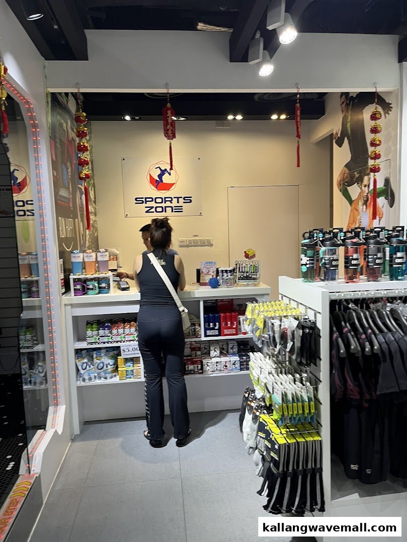 A customer at the counter of a shop featuring 'Sports Zone' branding, with sports nutrition and apparel.