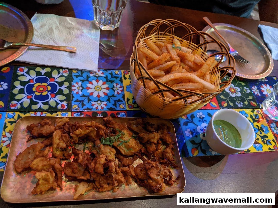A vibrant table setting with a basket of seasoned fries, a plate of crispy fritters, and green chutney.