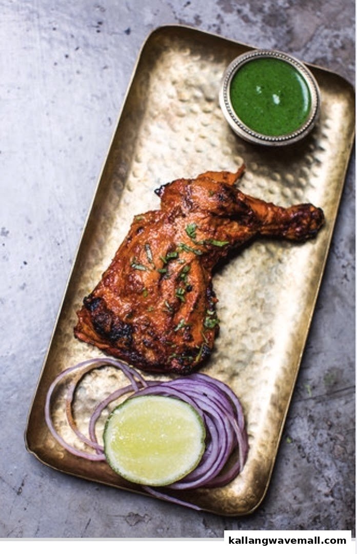 A vibrant tandoori chicken leg quarter served on a golden tray with green chutney, lime, and red onions.