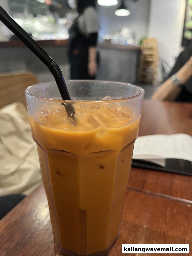 A refreshing iced Thai milk tea with a straw on a wooden table inside Sanook Kitchen.