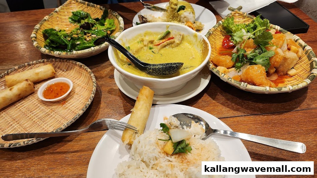 A table laden with various Thai dishes including green curry, spring rolls, and stir-fried vegetables.