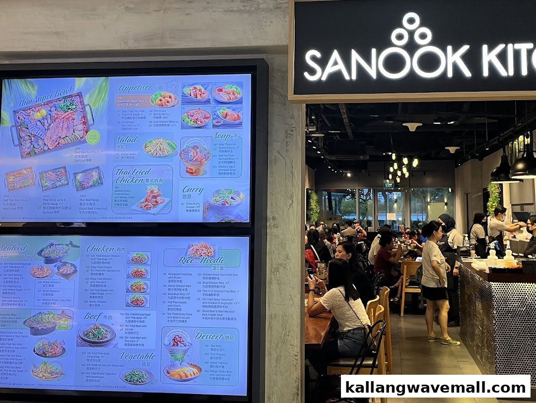 A vibrant digital menu board displaying Thai dishes next to the bustling entrance of Sanook Kitchen.