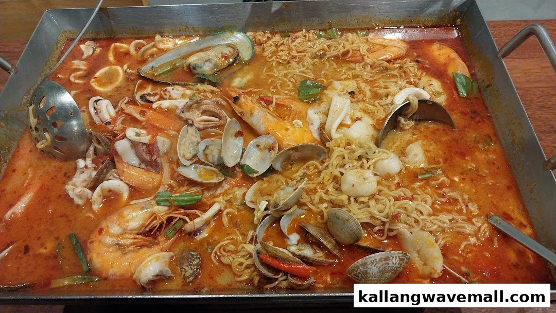 A large pan of vibrant Thai seafood tom yum noodles with prawns, mussels, clams, and squid.