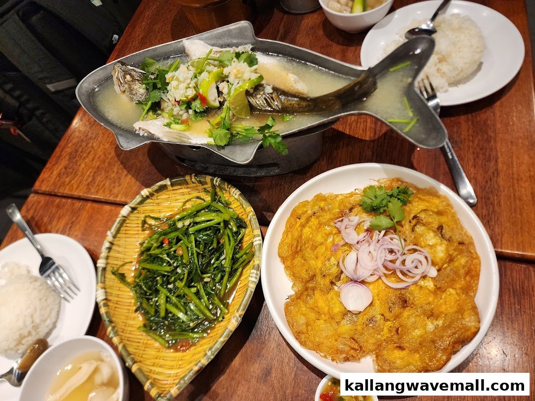 A table laden with delicious Thai dishes including steamed fish, stir-fried vegetables, and a crispy omelette.