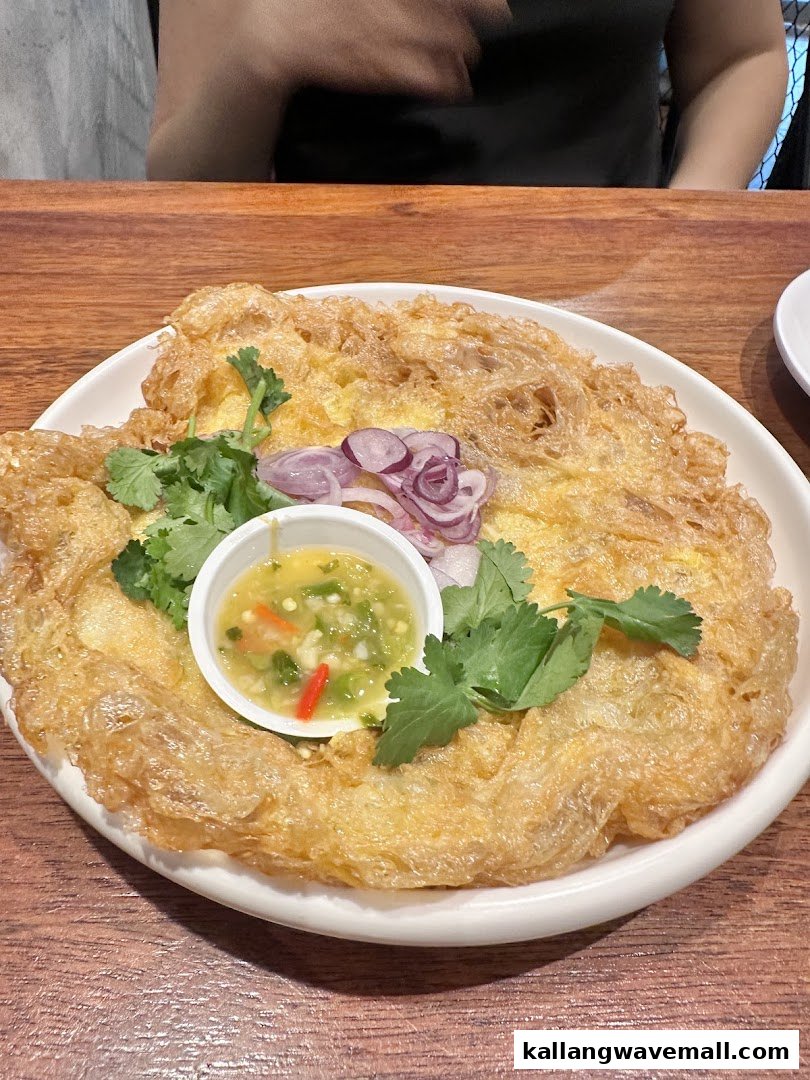 A crispy Thai-style omelette served with a spicy dipping sauce, fresh herbs, and sliced red onions.
