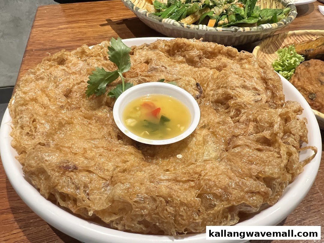A large, crispy golden-brown omelet or fried dish served with a small bowl of dipping sauce.