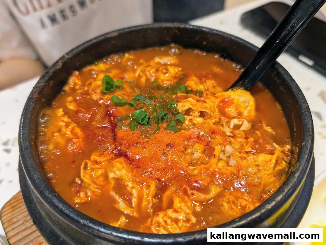 A vibrant, bubbling Korean stew with egg and green onions in a black stone pot.
