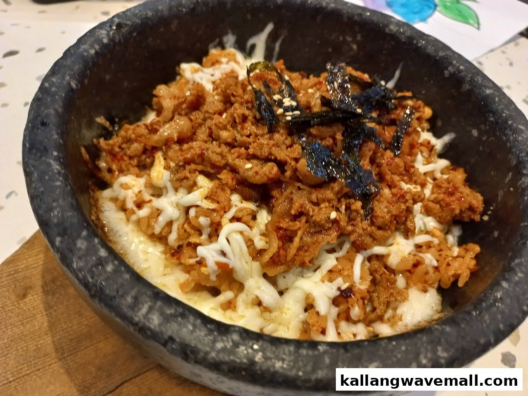 A close-up of a sizzling Korean hot stone pot dish with spicy meat, melted cheese, and seaweed.