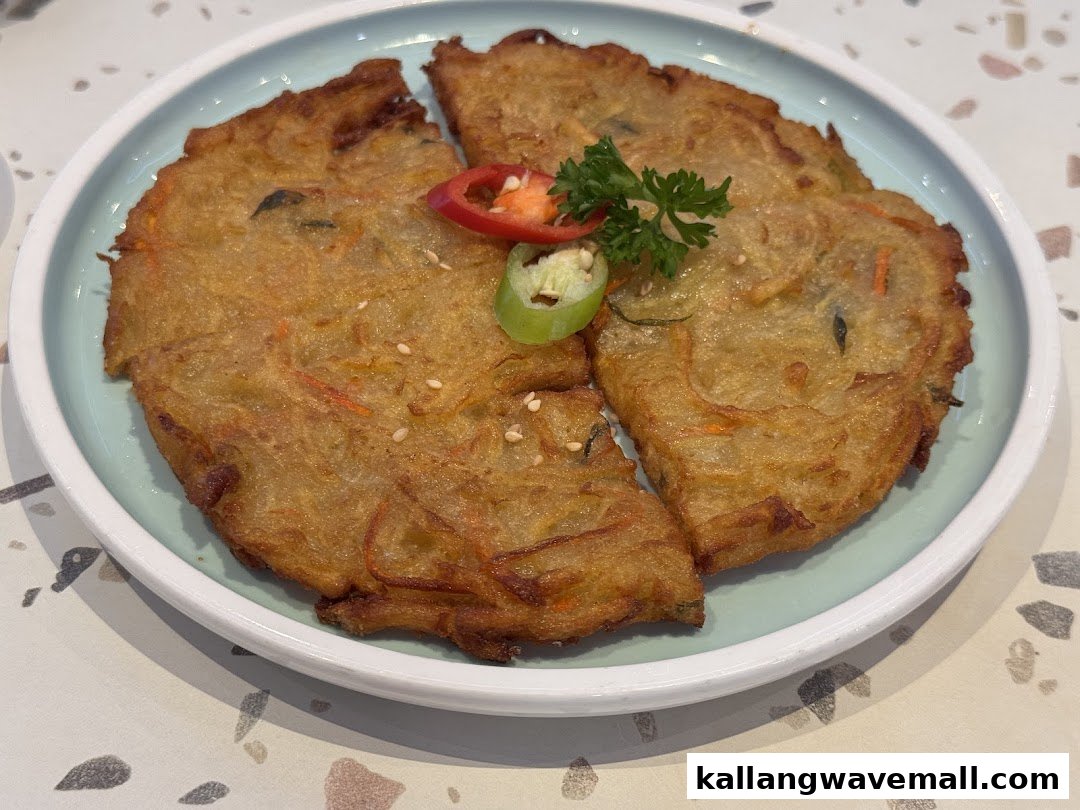 A golden-brown Korean pancake (jeon) garnished with chili and parsley on a light blue plate.