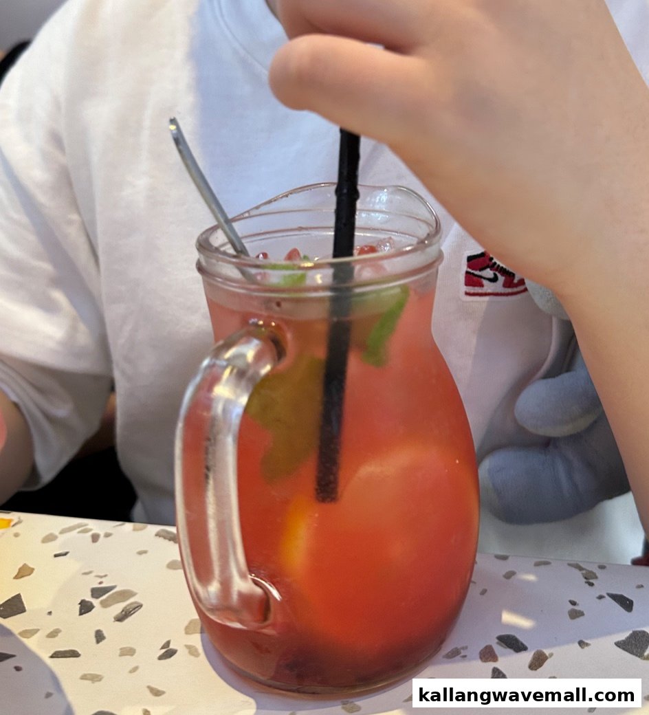 A person enjoying a refreshing red drink with mint and lemon in a glass pitcher.