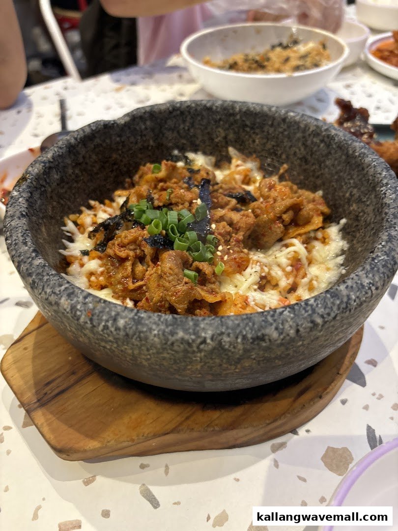 A close-up of a delicious Korean dish with melted cheese and meat in a hot stone bowl.
